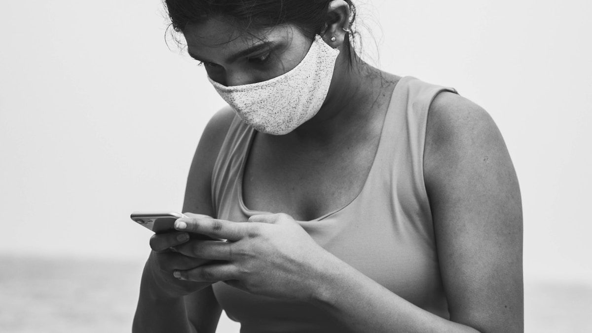 Nainen maskissa käyttää älypuhelinta