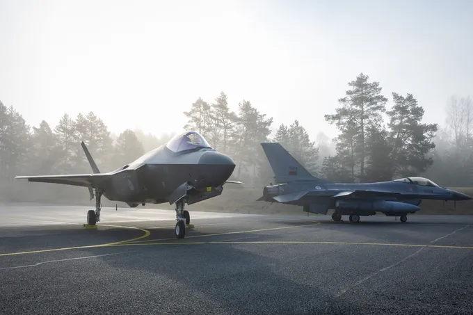 Hollantilainen F-35-hävittäjä ja portugalilainen F-16-hävittäjä seisovat asfaltilla sumuisena aamuna. Taustalla on mäntymetsää.