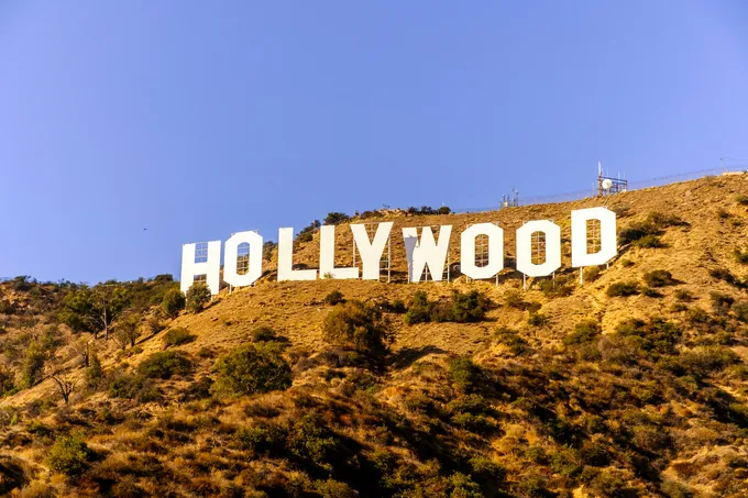 Valkoinen Hollywood-kyltti kuivan, pensaikkoisen kukkulan rinteessä sinistä taivasta vasten.